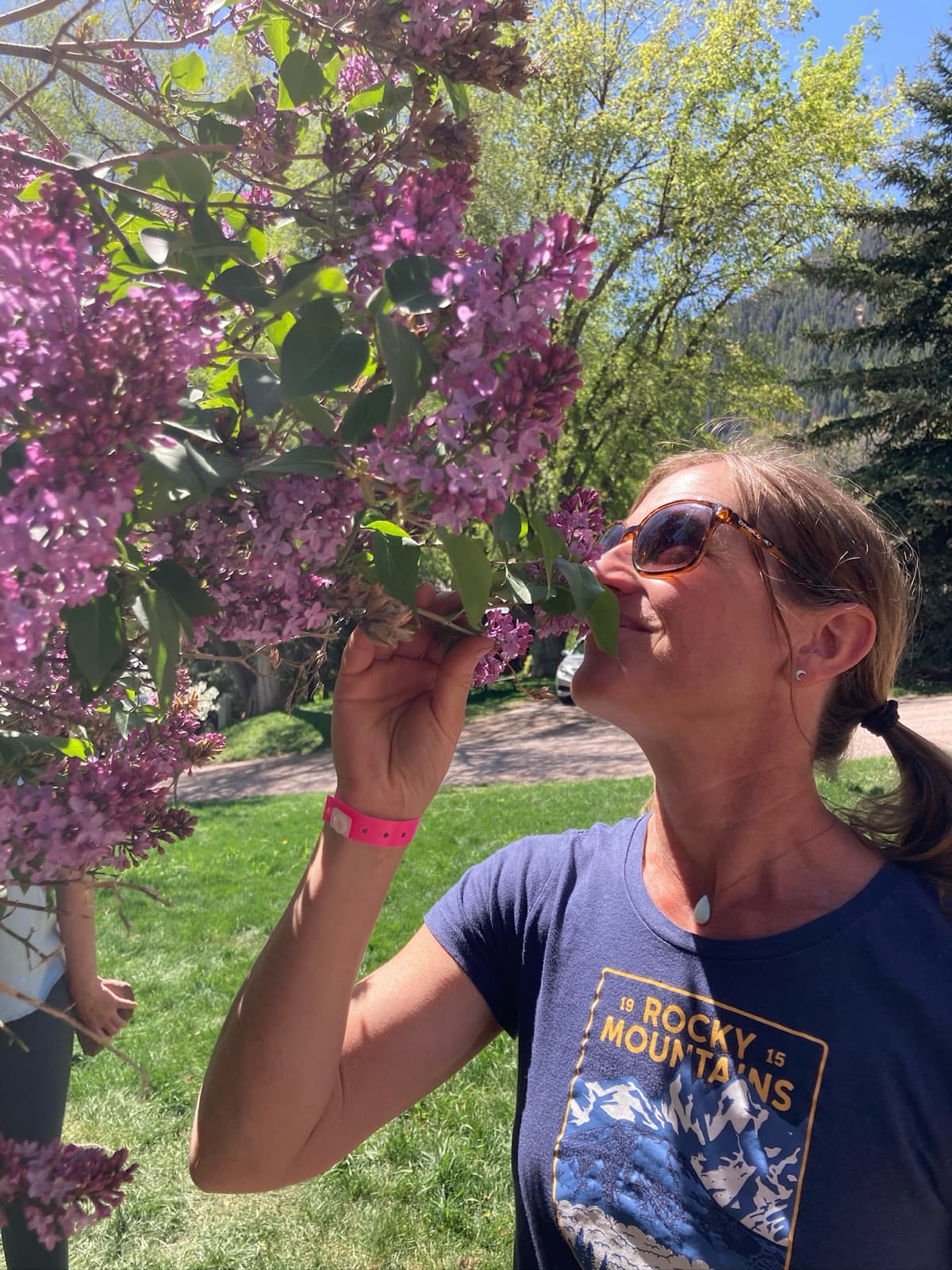 Ms. Rachel breathing in a branch of lilac blossoms in the spring sunshine