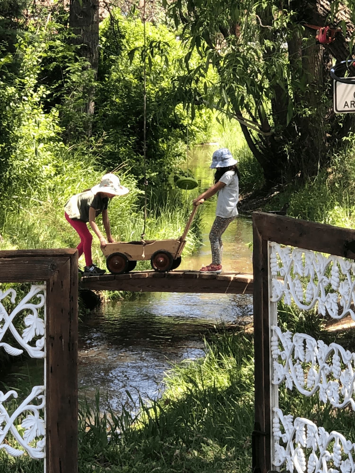Two children wheeling a wooden wagon across the creek bridge