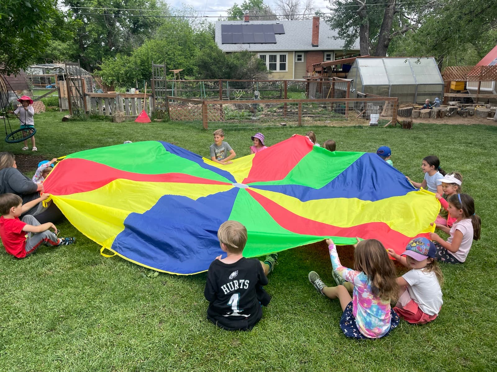 The rainbow parachute stretched wide, a ring of children holding on
